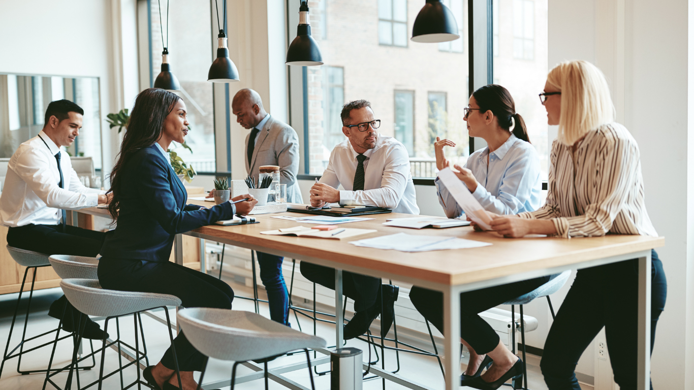 Colleagues seated at a table in an office, participating in a conversation about conflict management and workplace trust.