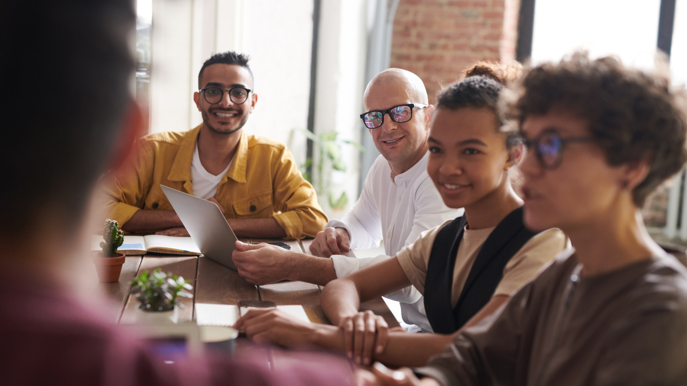 A group of diverse professionals at a table, engaged in a collaborative discussion with a laptop, highlighting a peaceful mediation environment.